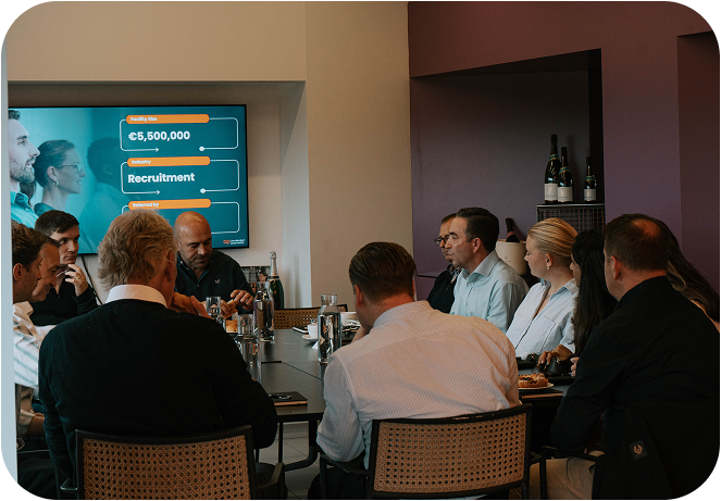 Business meeting around a conference table with a presentation screen showing recruitment figures